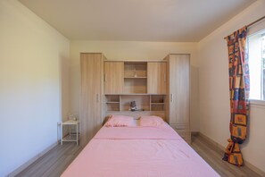 A bedroom with a bed, a nightstand, a wardrobe, and a window with curtains. - Villa "Apartment with Garden" with Mountain View, Private Terraces, and Air Conditioning (Aléria)