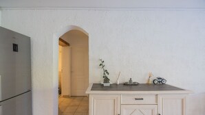 A kitchen with a refrigerator, cabinets, and a small table with decorative items. - Villa "Apartment with Garden" with Mountain View, Private Terraces, and Air Conditioning (Aléria)