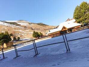 Estância de esqui com um chalé de madeira, encostas cobertas de neve e um céu azul límpido.