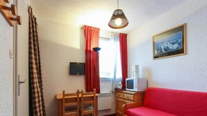 Ein kleiner Raum mit einem Holztisch, einem roten Sofa, einem Fernseher, einer Mikrowelle und einem Gemälde an der Wand.