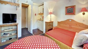 A bedroom with a bed, a television, a bedside table, a lamp, and a wall-mounted picture. - Family Alpine Stay in Risoul (Risoul)