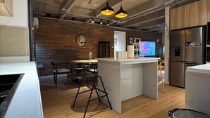 Una cocina moderna con una isla central, una zona de comedor con sillas, un refrigerador y un televisor.