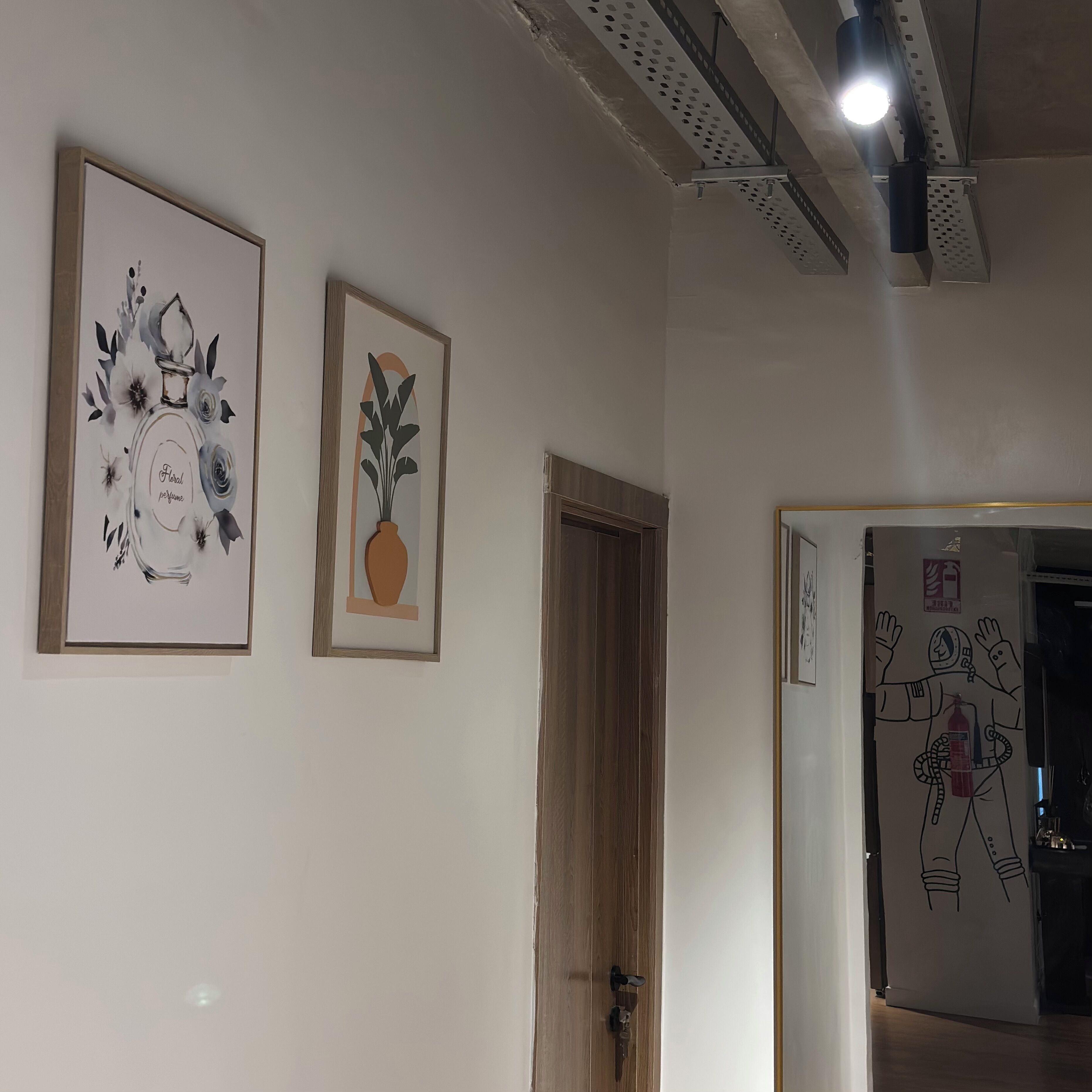 A hallway with two framed artworks, a wooden door, and a door with a fire safety sign.