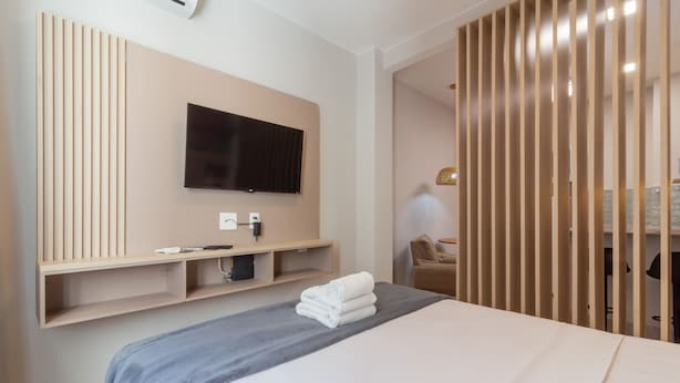 Et hotelværelse med en seng, et ophængt tv, en væg beklædt med træpaneler og et lille siddeområde.