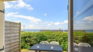 An outdoor patio with a table and chairs, a wooden fence, and a view of the sea. - Brittany Flat, Beach & Pool (Saint-Nic)
