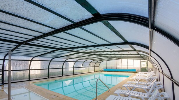 A covered swimming pool with clear water, surrounded by white lounge chairs, and a bench along the edge. - Brittany Flat, Beach & Pool (Saint-Nic)