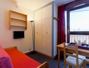 Una habitación con cama, escritorio, silla, armario, televisor y ventana con vistas.