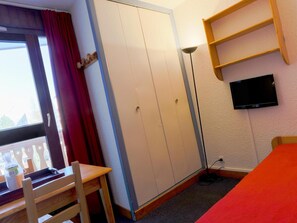 A room with a bed, a desk, a wardrobe, a TV, and a window with curtains. - Cosy Romantic Studio in Les Deux Alpes (Les Deux Alpes)