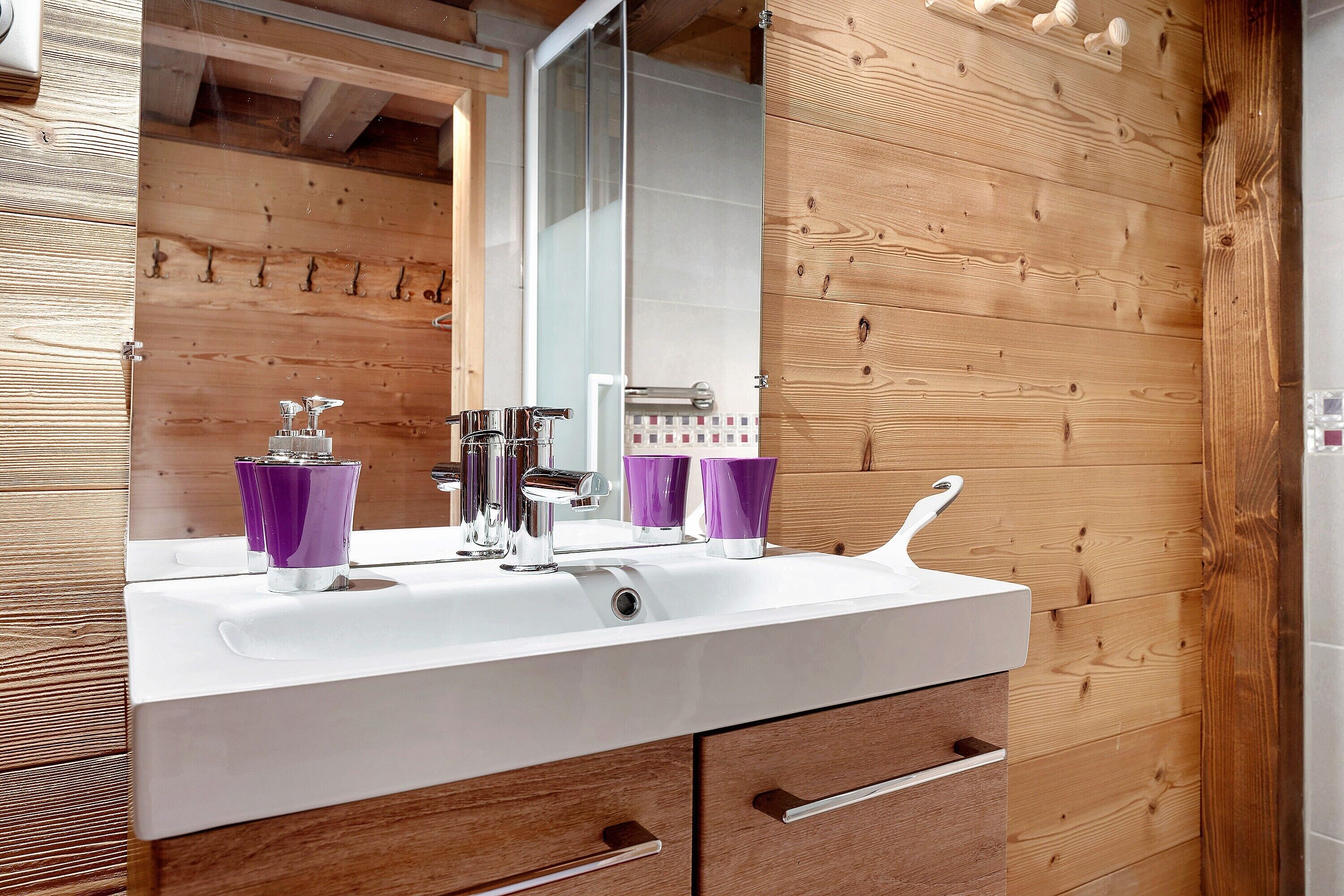 A bathroom with a wooden wall, a white sink, and two purple cups.