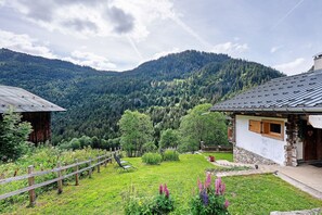 Un rustico albergo di montagna con una recinzione in legno, un giardino fiorito e vista su dolci colline boscose.