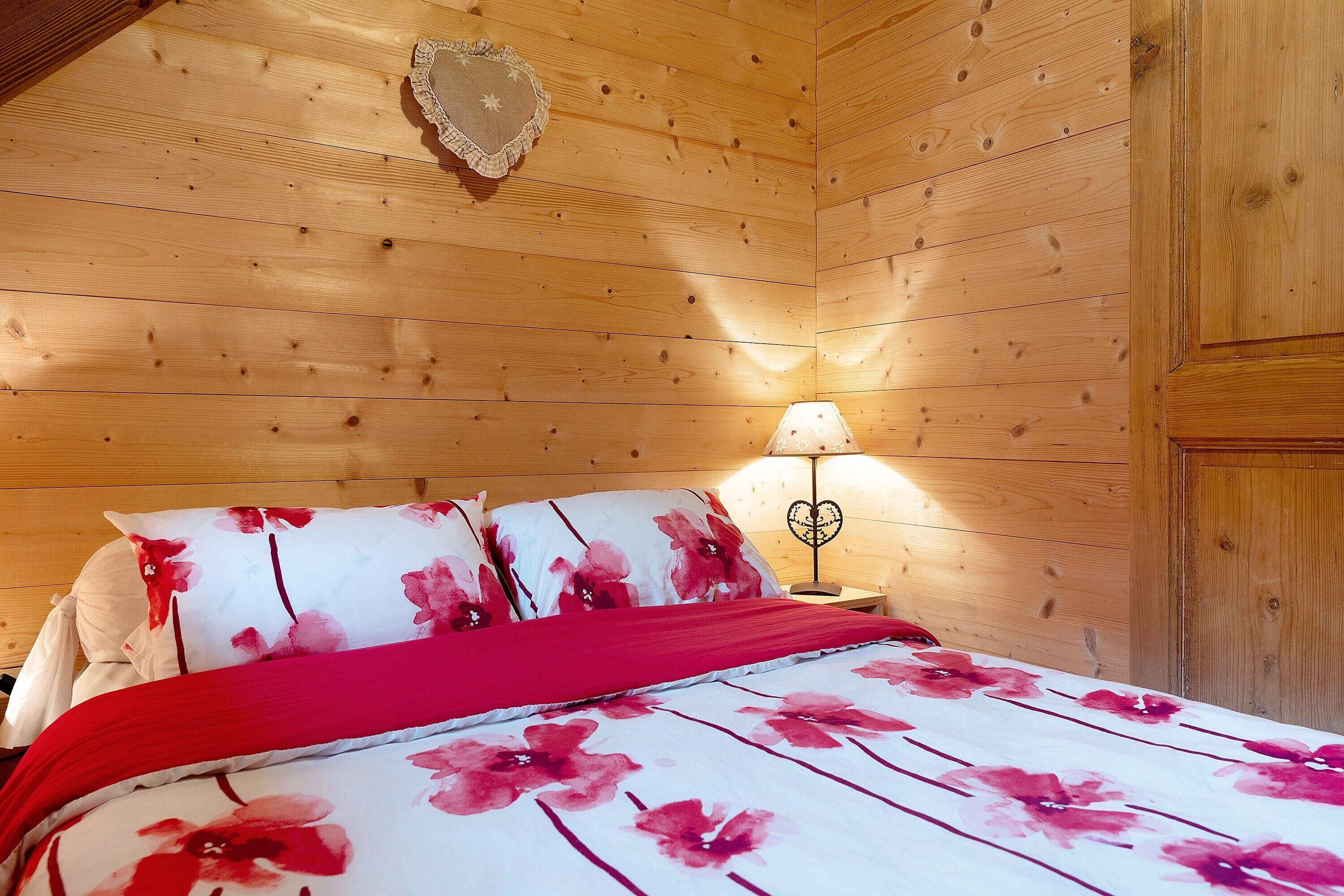Une pièce aux murs lambrissés, comprenant un lit, une table de chevet et une lampe fixée au mur.