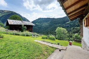 Un bâtiment rustique en bois, avec un chemin de pierre menant à une terrasse en bois qui offre une vue imprenable sur une vallée verdoyante.