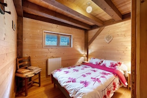 Camera da letto in una baita di legno, con un letto, una sedia, una finestra e un termosifone.