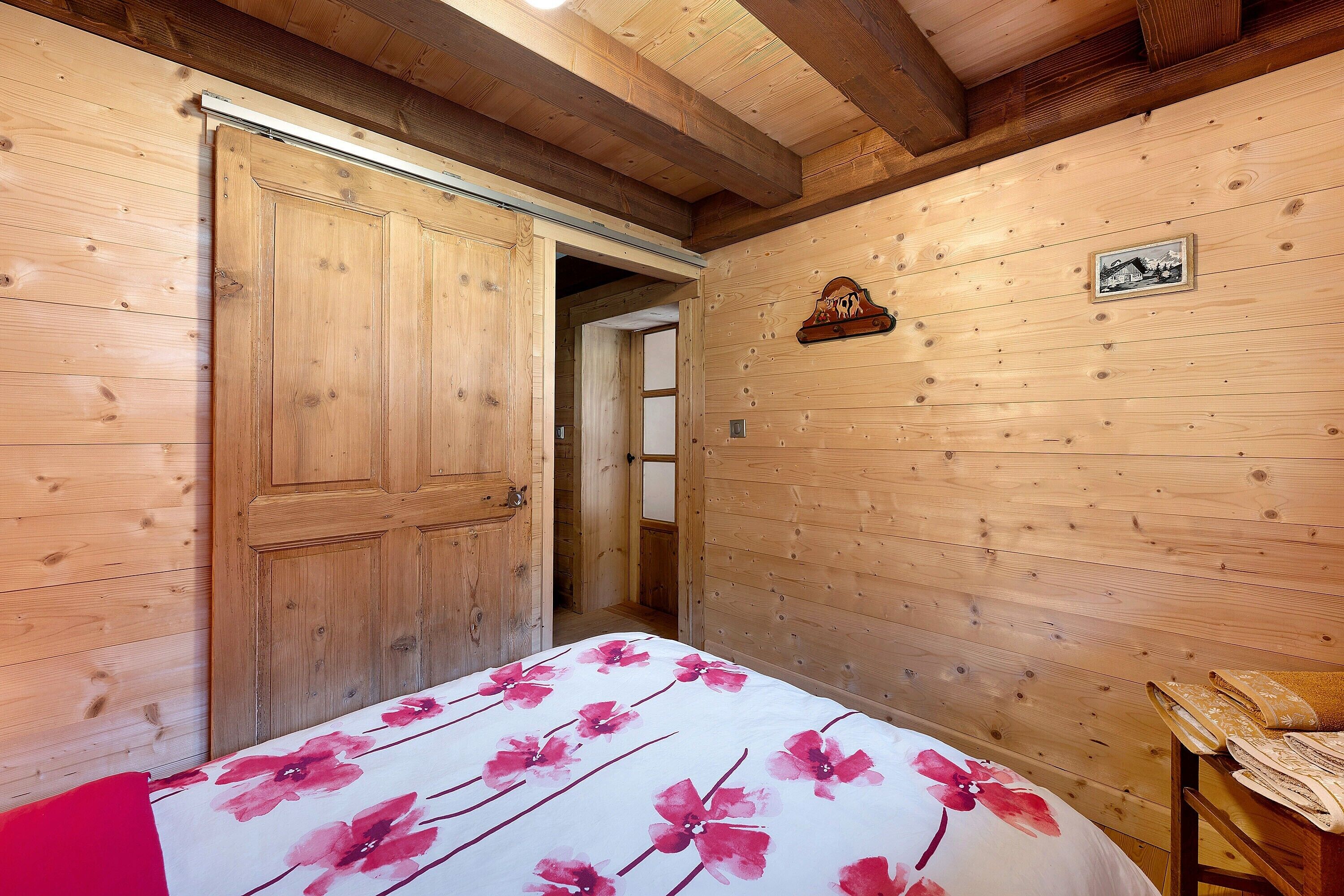 Una habitación con paneles de madera, una cama, una puerta de madera y una mesita con una toalla.