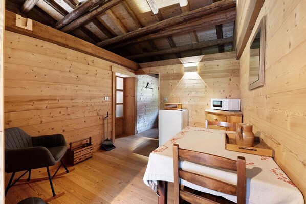 L’intérieur d’une cabane en bois, avec une table à manger, des chaises, un four à micro-ondes et un balai.