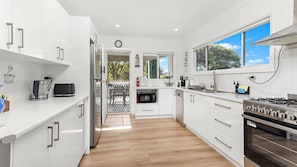 Una cocina moderna con armarios blancos, una estufa de acero inoxidable y vistas al exterior a través de un amplio ventanal.