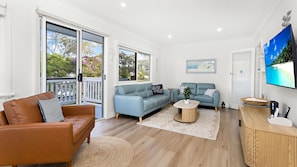 A living room with a brown leather sofa, a blue sofa, a coffee table, and a TV on the wall. - Sunset Sanctuary - Pet Friendly - 5 Mins Walk to Beach (Sanctuary Point)