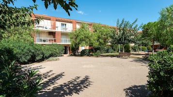 A courtyard with a building featuring balconies, surrounded by greenery and trees.