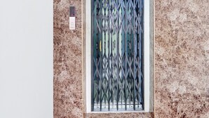 Una puerta con una reja metálica, un muro de mármol y un pequeño dispositivo electrónico en la pared.