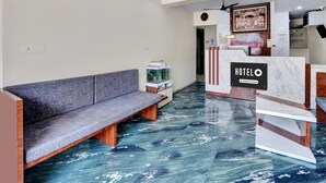 Zona de recepción de un hotel con suelo de mármol, un mostrador de recepción, un sofá y un cuadro en la pared.