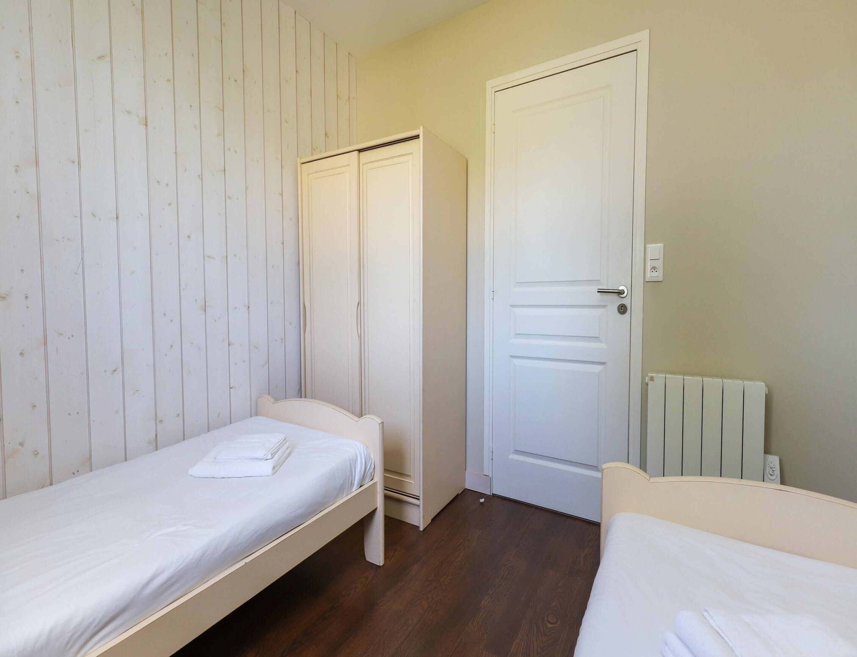 A bedroom with two single beds, a wardrobe, a door, and a radiator.