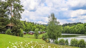 A rural setting with a lake, green fields, and a row of cabins. - 6-person Wooden Chalet in Correze (Meyrignac-l'Eglise)