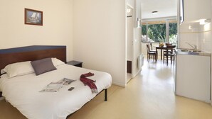 A hotel room with a bed, a small bedside table, a dining area with a table and chairs, and a kitchenette. - Studio in the Heart of Nature (Vallon-Pont-d'Arc)