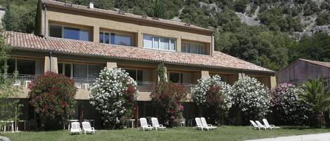 A two-story building with a tiled roof, a balcony, and white lounge chairs in front.