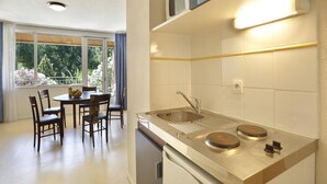 A compact kitchen with a sink, stove, and dining area with chairs and a table. - Studio in the Heart of Nature (Vallon-Pont-d'Arc)