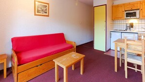 A compact living space with a red sofa, a small wooden table, and a kitchenette with wooden cabinets and a microwave. - Studio in Les Deux Alpes With Balcony (Les Deux Alpes)