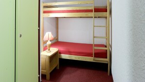 A bunk bed with a red mattress, a wooden nightstand with a lamp, and a ladder. - Studio in Les Deux Alpes With Balcony (Les Deux Alpes)