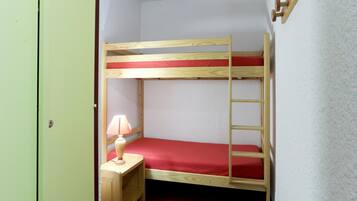 A bunk bed with a red mattress, a wooden nightstand with a lamp, and a ladder.