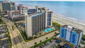 Een hoog hotel met meerdere balkons, een zwembad en uitzicht op het strand.