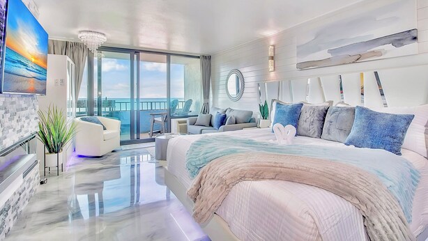 Een moderne hotelkamer met een groot bed, een balkon met uitzicht, een zithoek en een groot schilderij.