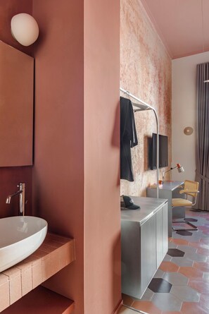 Un baño moderno con un espejo grande, una lámpara redonda, un lavamanos, un mueble de tocador, una silla y una televisión.