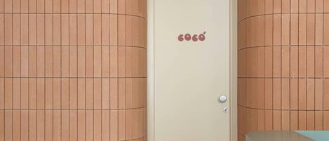 Una habitación con una pared curva, una puerta con picaporte, una mesita con jarrón y taza, y una silla.