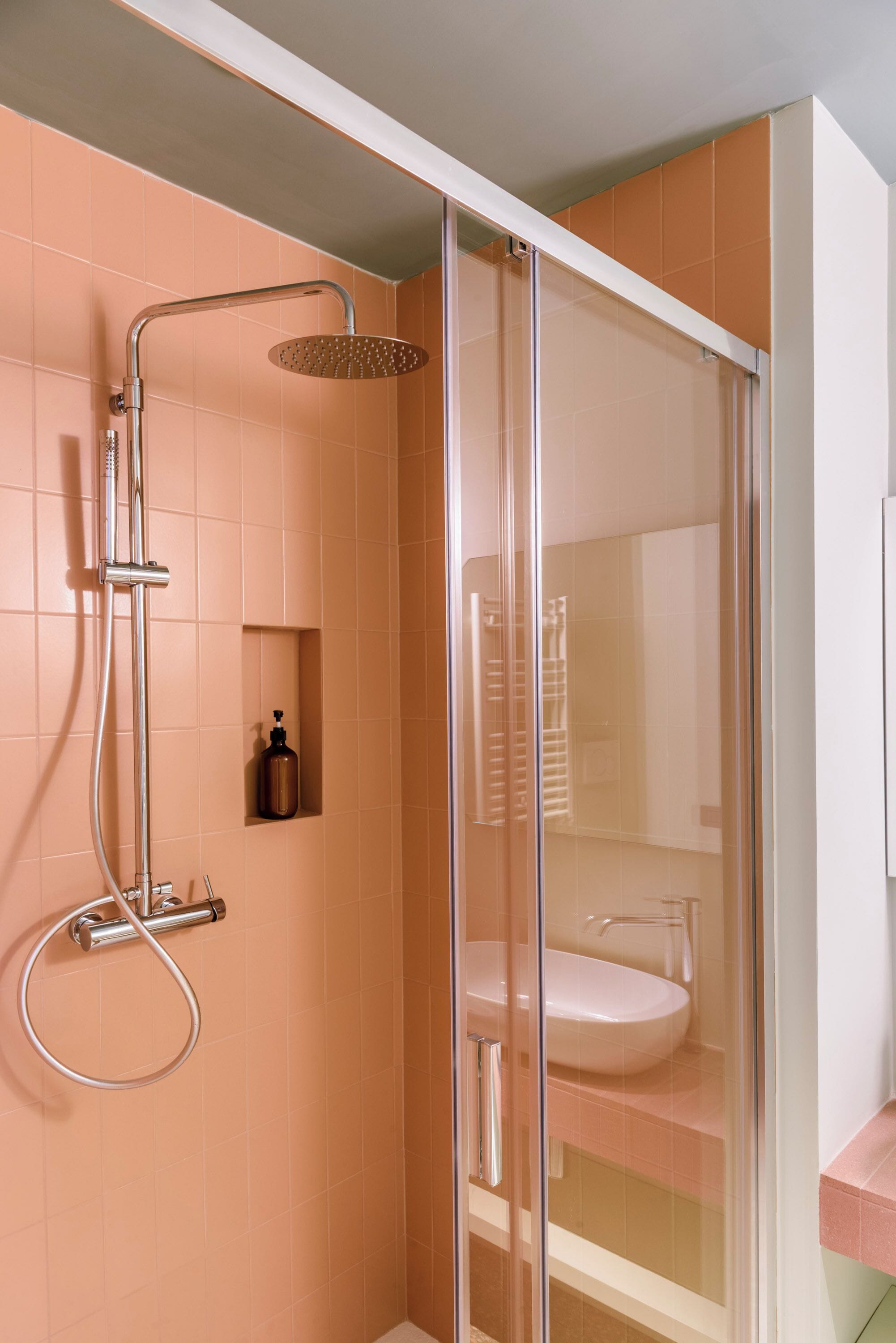 A modern bathroom with a glass-enclosed shower, a white sink, and a pink tiled wall.
