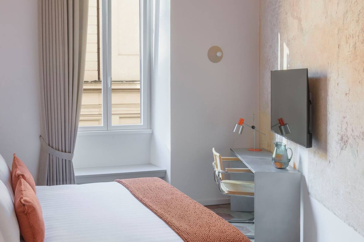 Une chambre d’hôtel avec un lit, un bureau, une télévision et une fenêtre avec des rideaux.