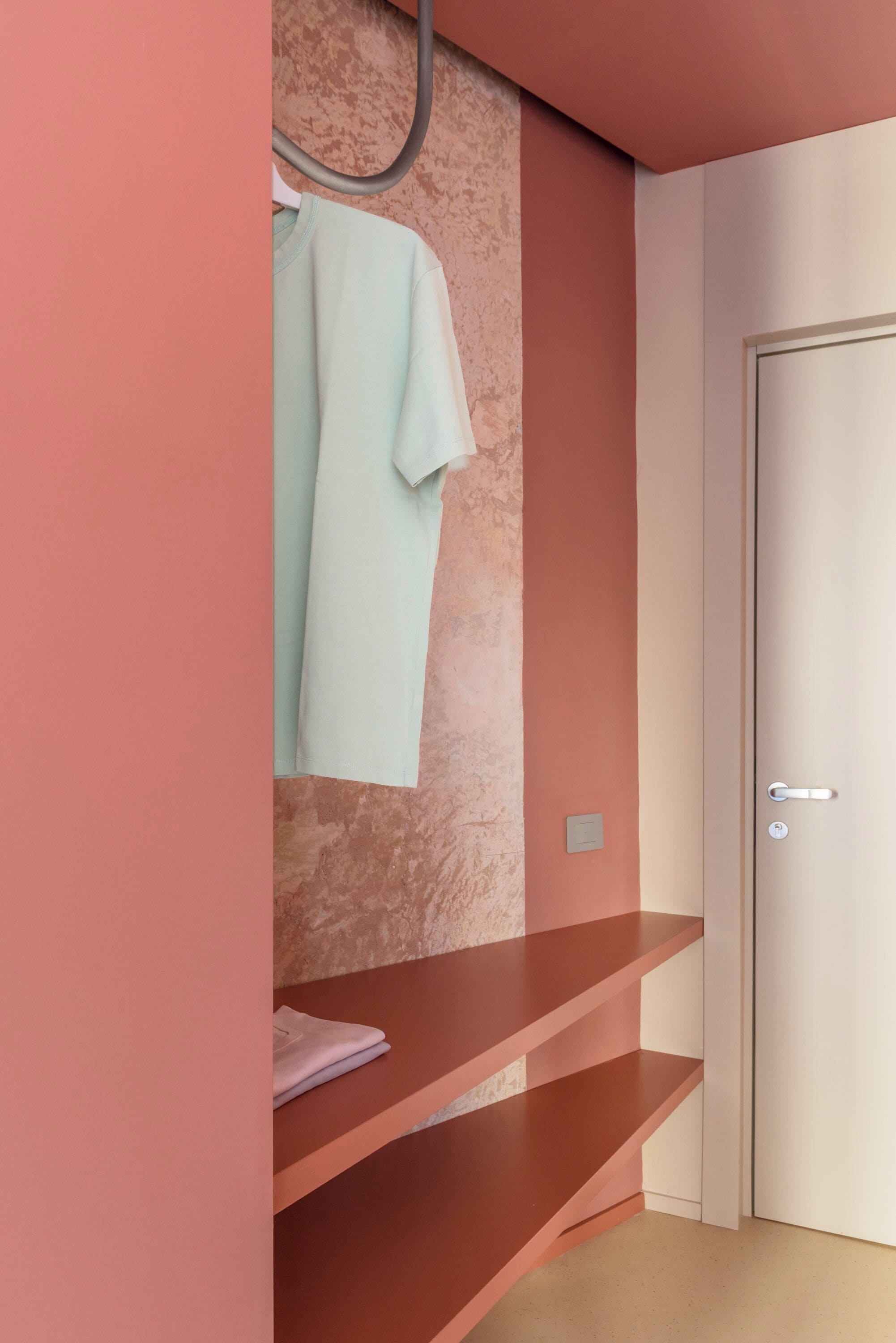 A room with a pink wall, a white door, and a towel hanging on a hook.