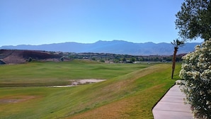 Camp de golf amb vista clara a muntanyes llunyanes, un camí pavimentat i un jardí ben cuidat.