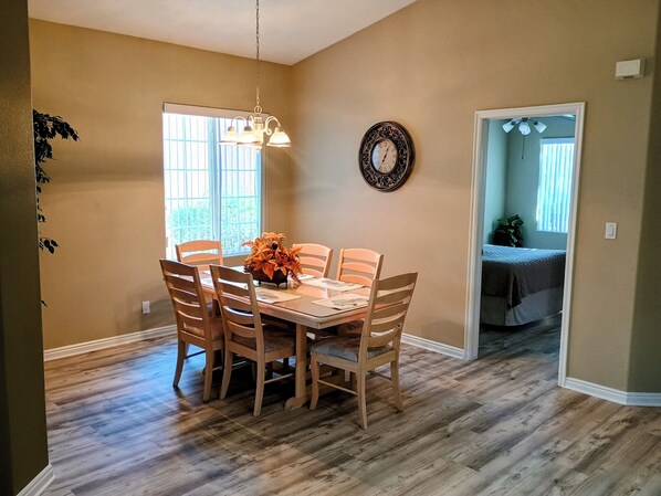 A dining area with a table, chairs, a chandelier, a clock, and a window with blinds.