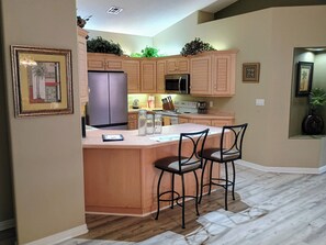 A kitchen with wooden cabinets, a refrigerator, a microwave, a stove, and a bar area with two chairs.