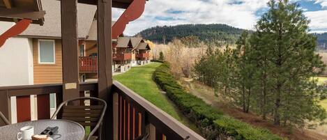 A balcony with a table, chairs, and a view of a forested area and buildings in the background.