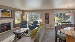 Una sala de estar con chimenea, dos sillones, un sofá, un comedor con mesa y sillas, y vistas a un campo de golf.