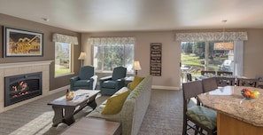 Una sala de estar con chimenea, dos sillones, un sofá, un comedor con mesa y sillas, y vistas a un campo de golf.