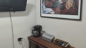 A room with a flat-screen TV mounted on the wall, a coffee maker, a framed artwork, and a small wooden table with a basket. - WLC Stay (Ayutuxtepeque)