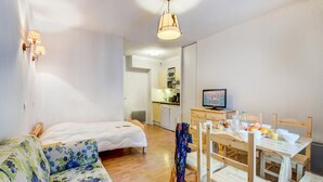 Ein gemütlicher Raum mit Bett, Schlafsofa, Esstisch mit Stühlen, Fernseher und Küchenzeile.