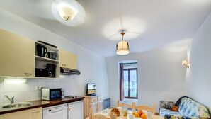 Eine kompakte Küche mit Mikrowelle, Toaster und Kaffeemaschine, ein Esstisch mit Stühlen sowie eine gepolsterte Sitzecke mit Blumenmuster.