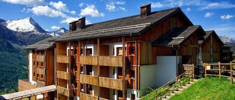 A wooden chalet with multiple balconies, a staircase, and a mountain backdrop.