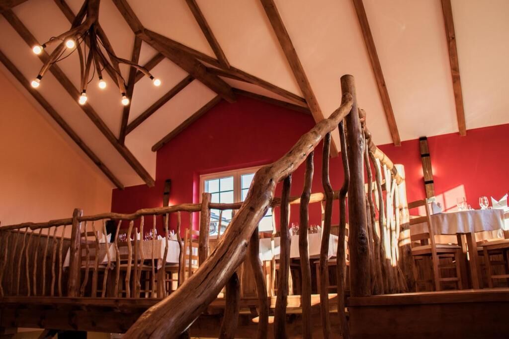 Een rustiek interieur met zichtbare houten balken, een rode wand en een eethoek met tafels en stoelen.